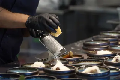 A server grating cheese over a dish
